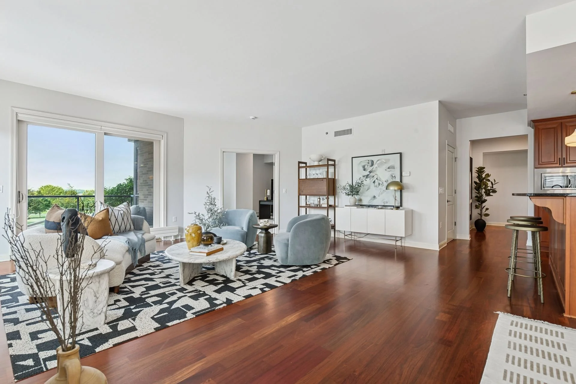 Spacious living room with white walls, large window with a view of greenery, and wooden floor.