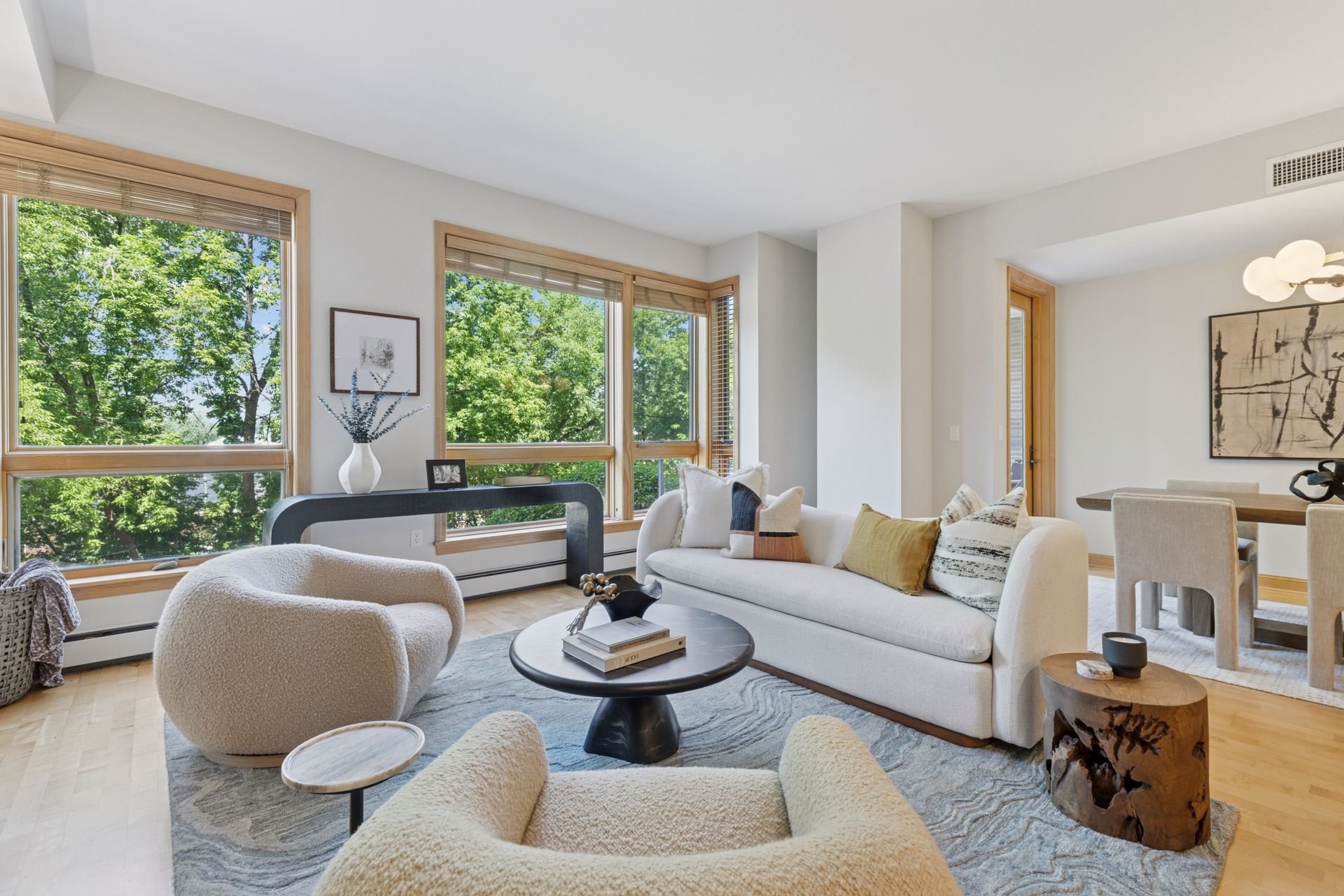Living room with large windows showing green trees.