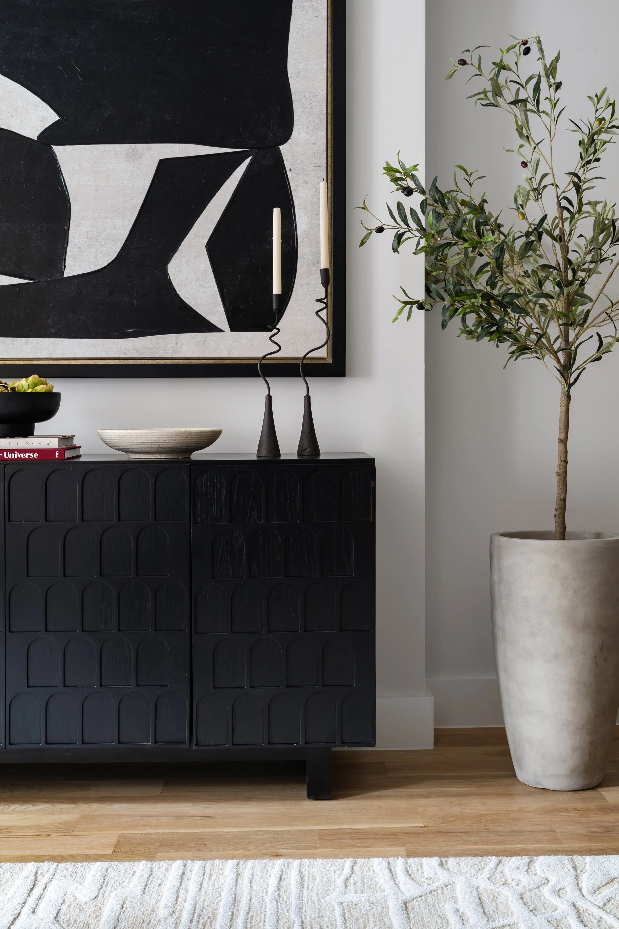 modern living area design featuring a black credenza abstract black and white painting asymmetrical candles and large potted plant