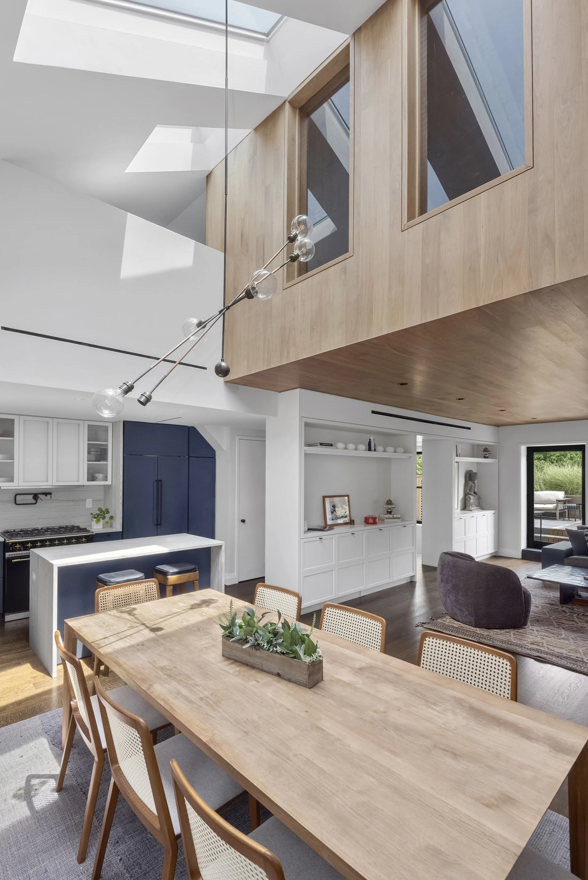 modern sun soaked dining area with light wood table and navy blue kitchen