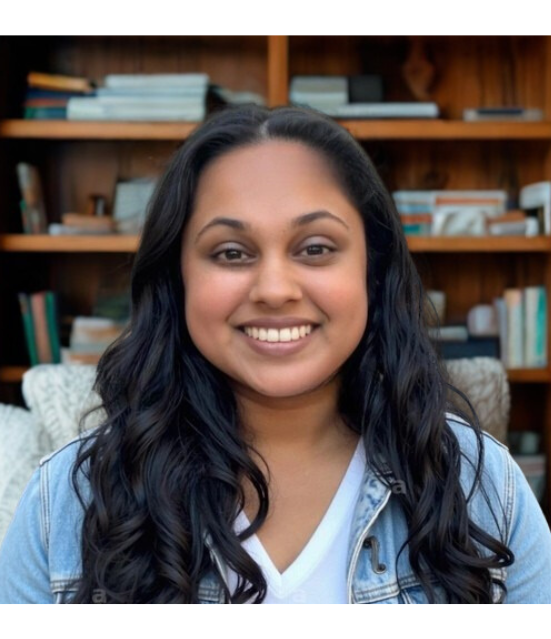 A woman with long, wavy black hair smiling at the camera, sitting in front of a wooden bookshelf filled with books.