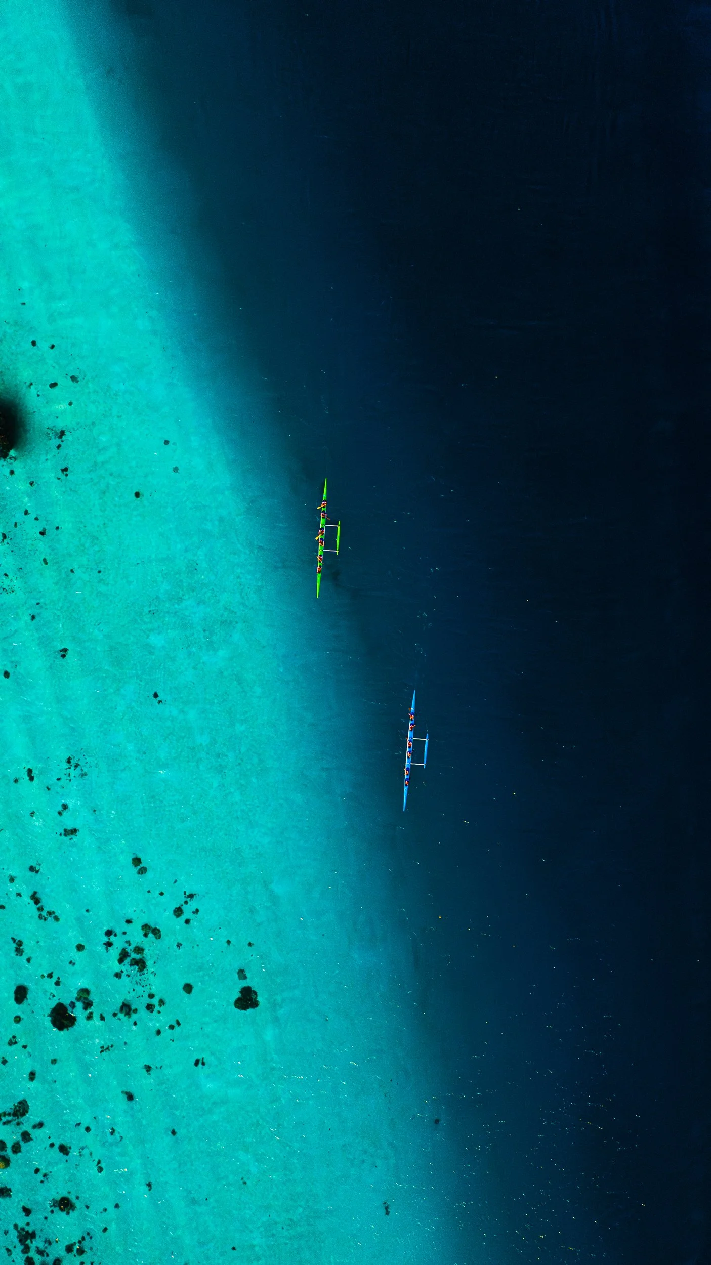 A professional drone image of Two Kayakers racing on a turquoise reef where it meets the dark blue ocean.


