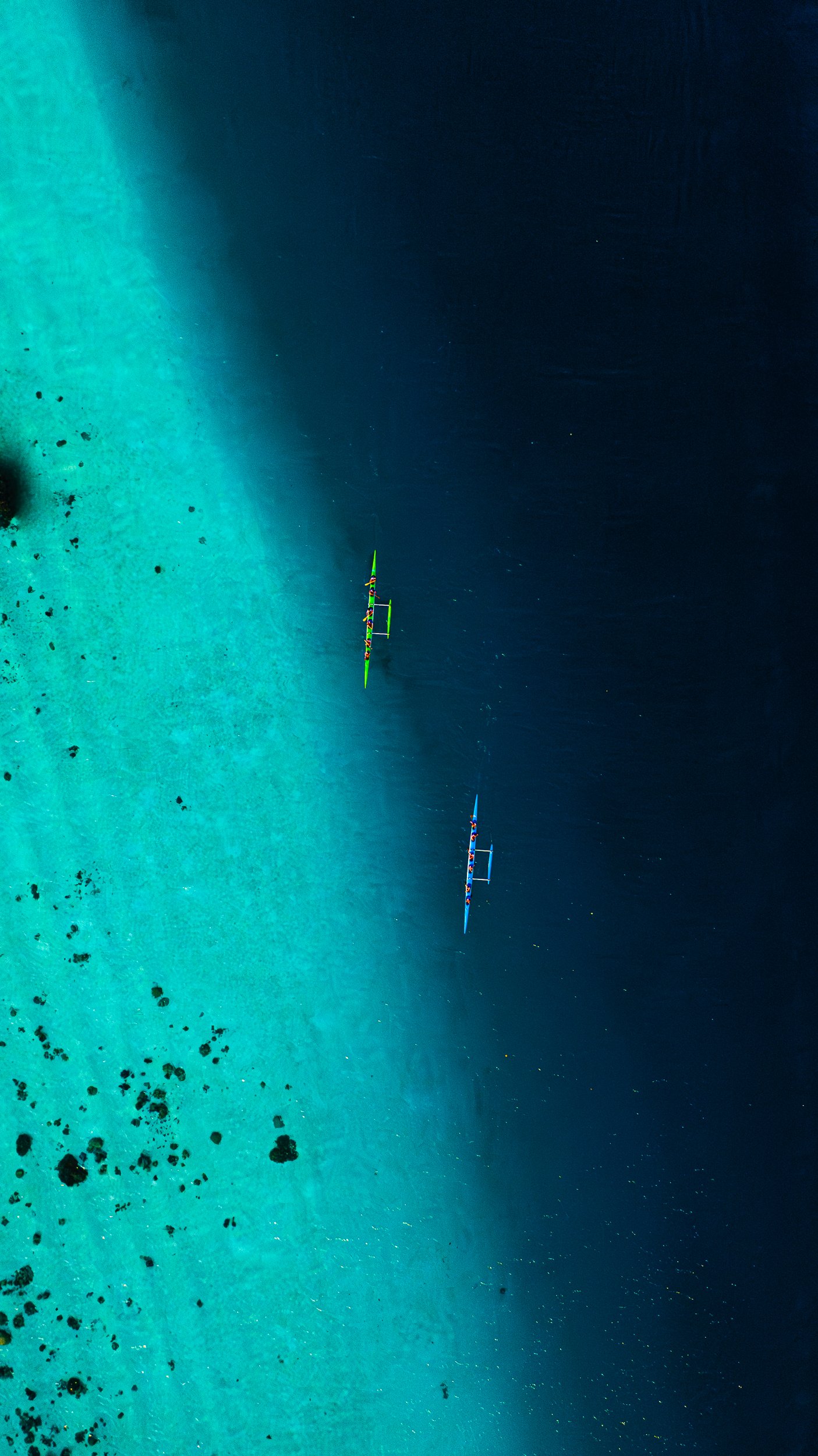 A professional drone image of Two Kayakers racing on a turquoise reef where it meets the dark blue ocean.  
