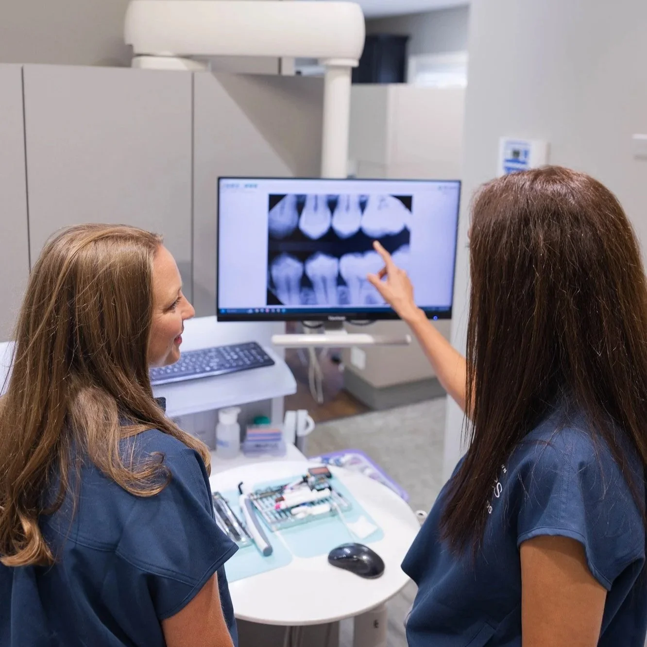 Two dental professionals reviewing a dental X-ray displayed on a computer monitor in a clinic setting.