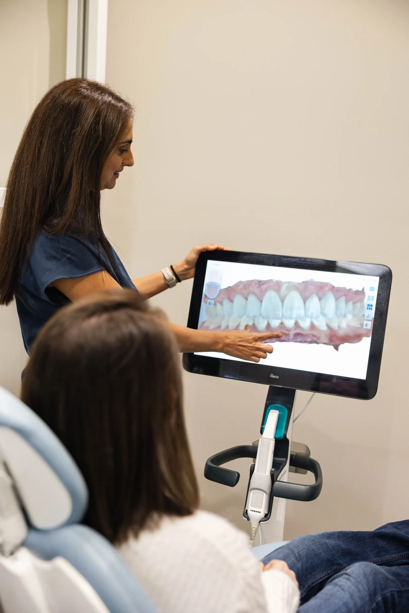 A dental professional showing a digital image of teeth on a monitor to a patient in a dental office.