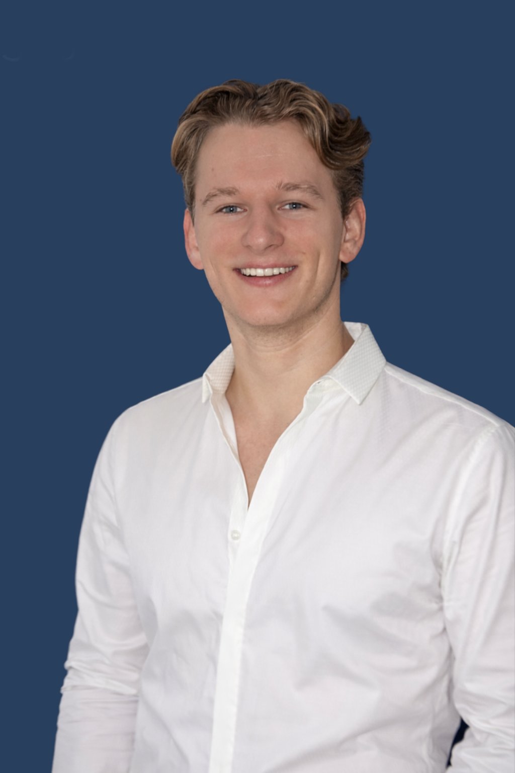Lächelnder junger Mann mit kurzen braunen Haaren, weißem Hemd, vor dunklem Blauhintergrund