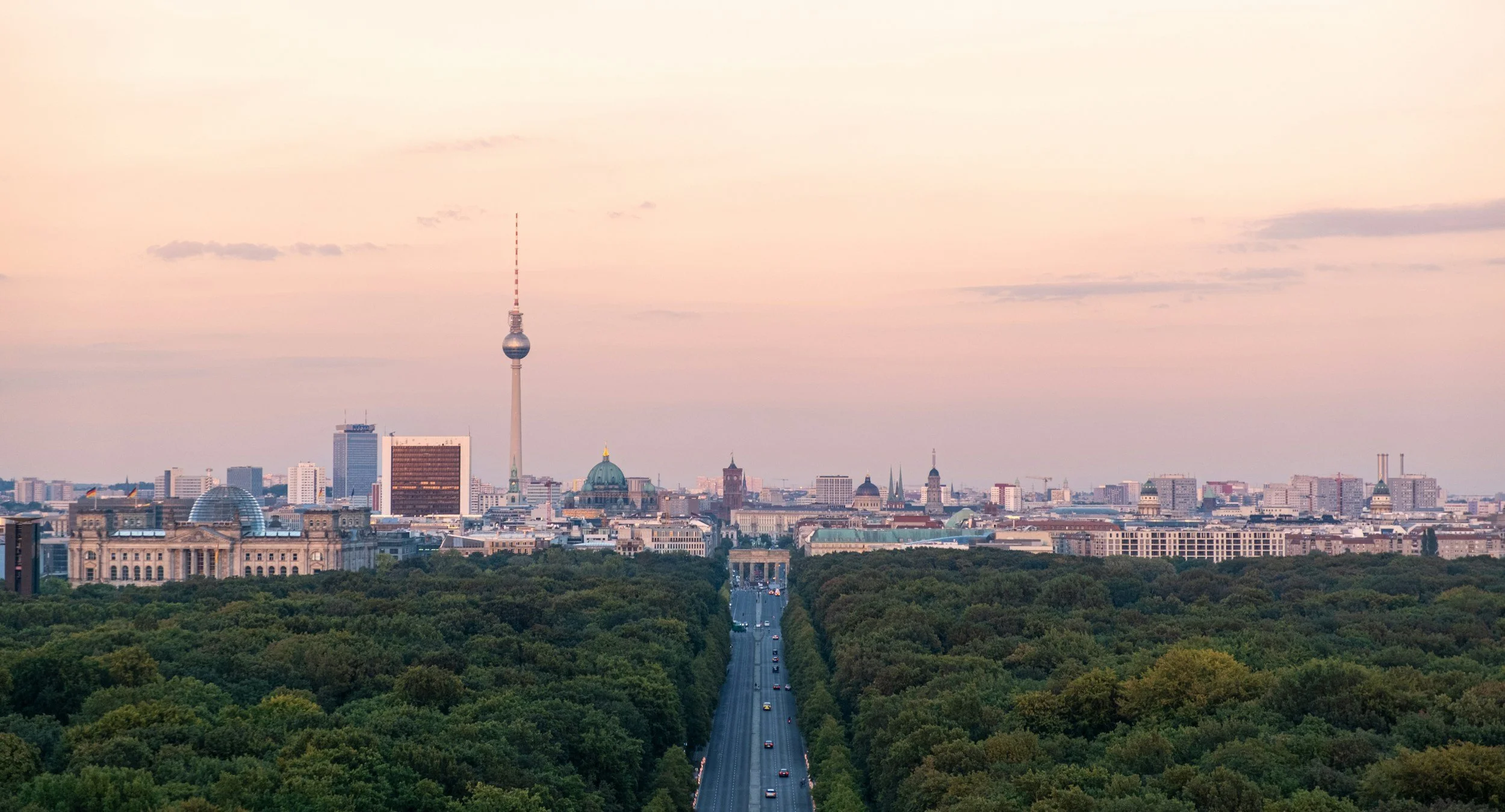 Blick auf die Berliner Skyline bei Sonnenuntergang, mit Fernmeldeturm, Regierungsviertel und viel Grünfläche im Vordergrund.