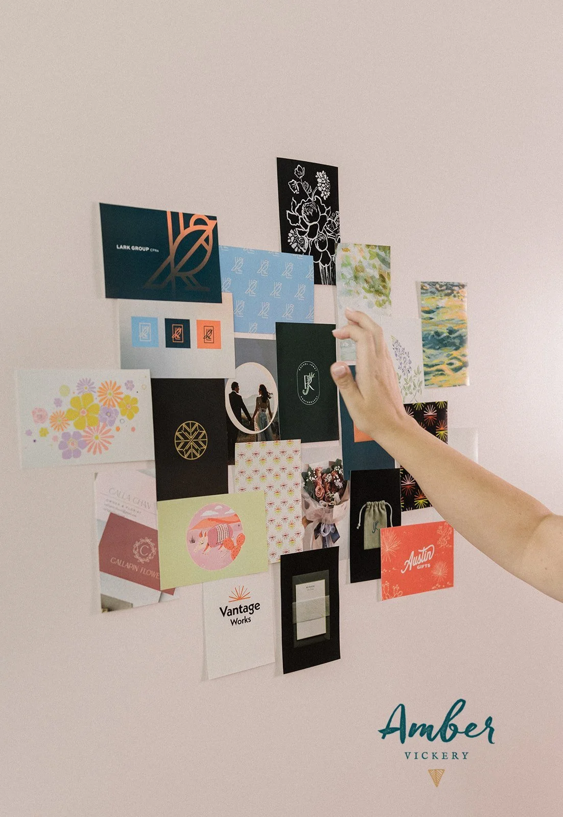 A person arranging a collage of various colorful cards and images on a white wall.