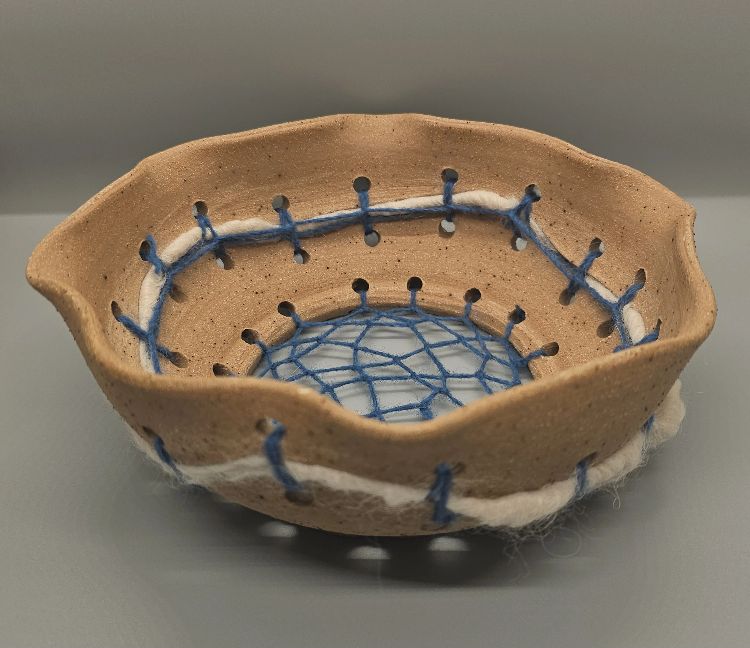 A ceramic bowl with blue and white string stitched inside, resembling a dreamcatcher design.