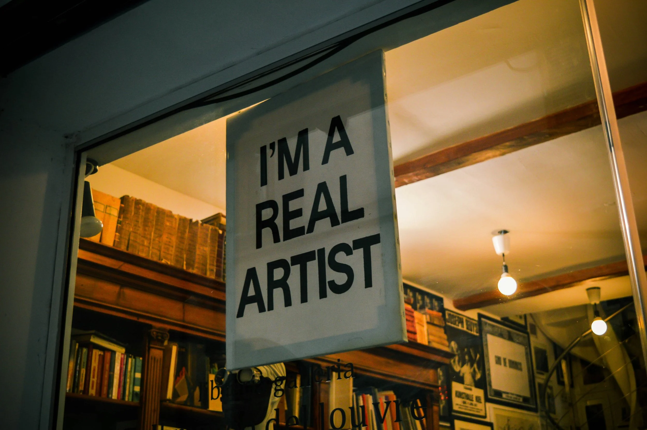A sign hanging inside a store or gallery reads 'I'M A REAL ARTIST'.