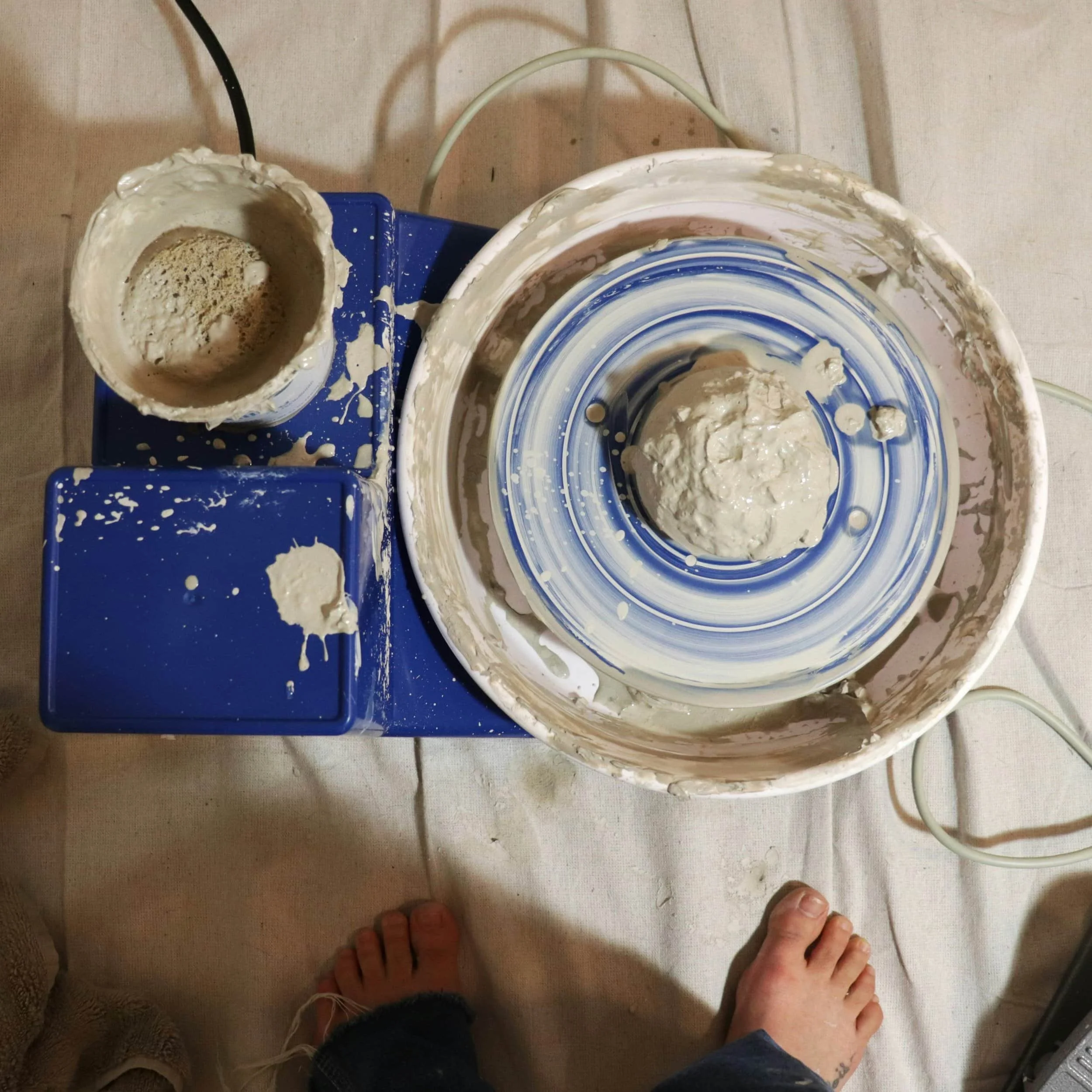 A blue pottery wheel with clay and water and a sponge.