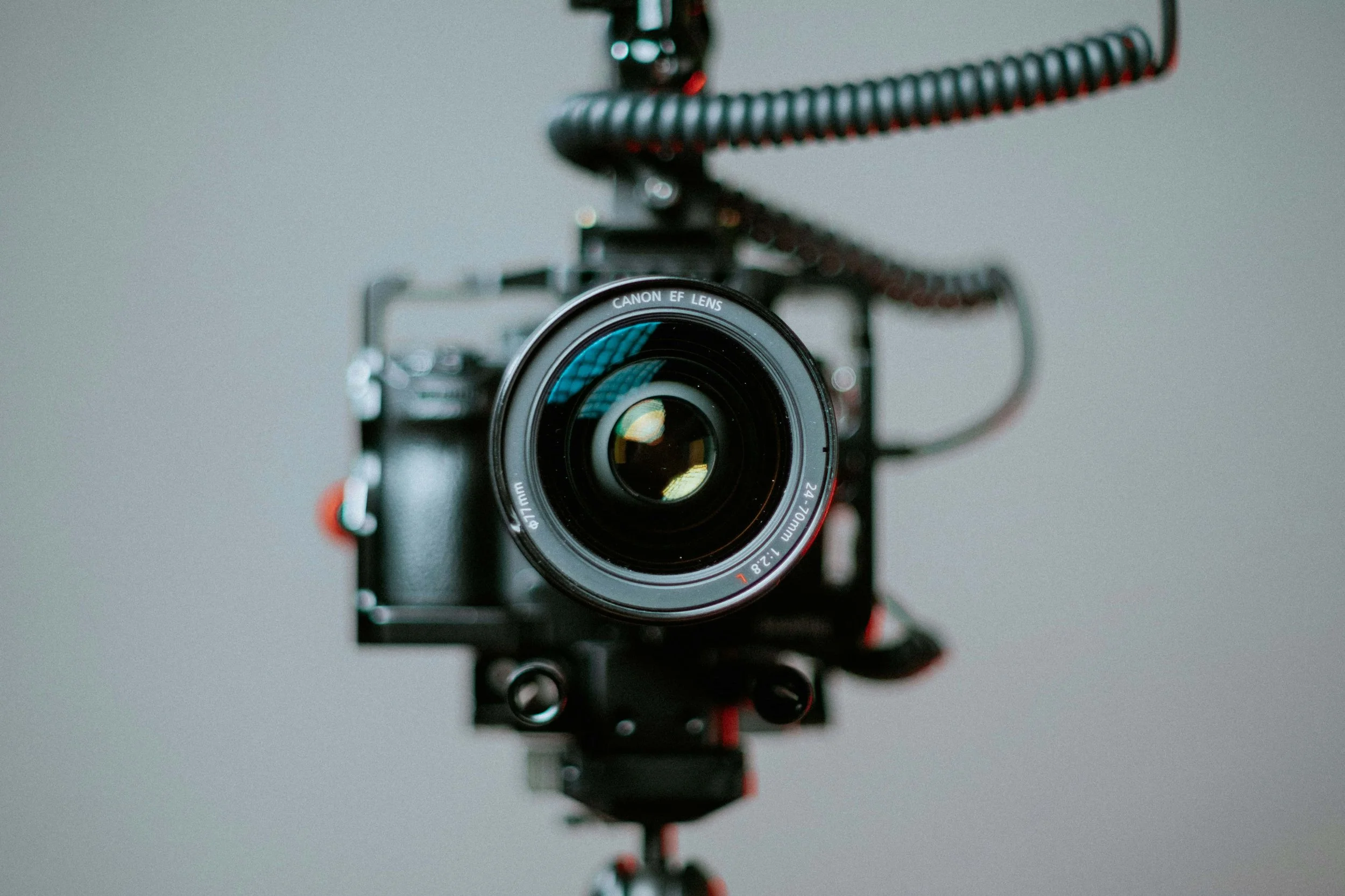 A camera mounted on a stabilizer, with the front lens facing the viewer, set against a blurred neutral gray background.