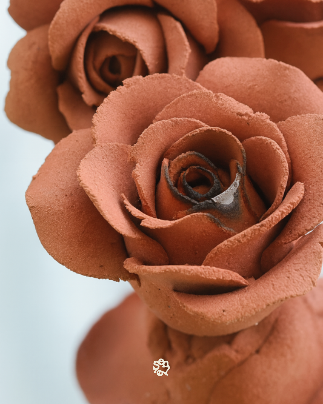 Close-up of two brownish, velvety roses, possibly made of clay or foam, with detailed petal textures.