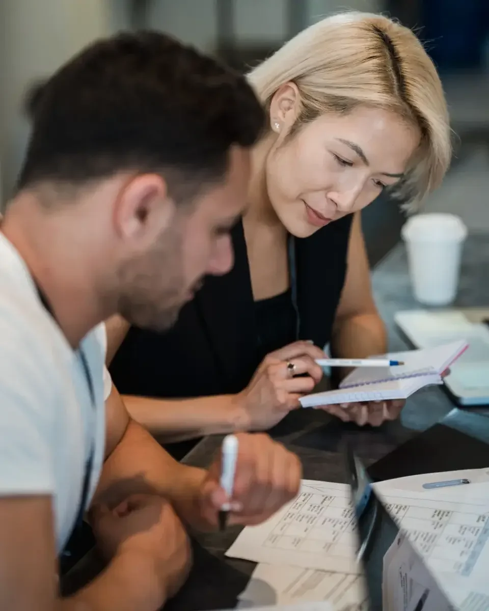 Two people with pens and notebooks reviewing documents