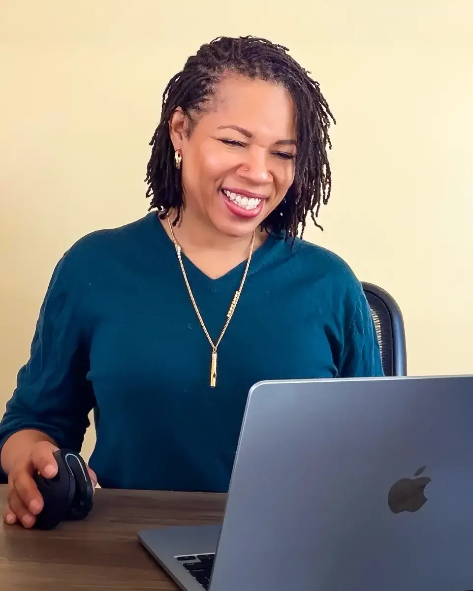 Kathering st her desk smiling working at her laptop
