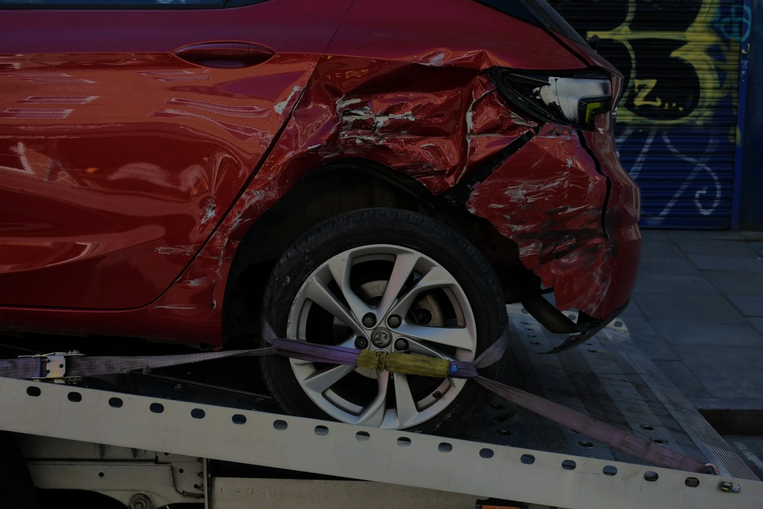 Red car with front-end damage, secured on a flatbed tow truck.