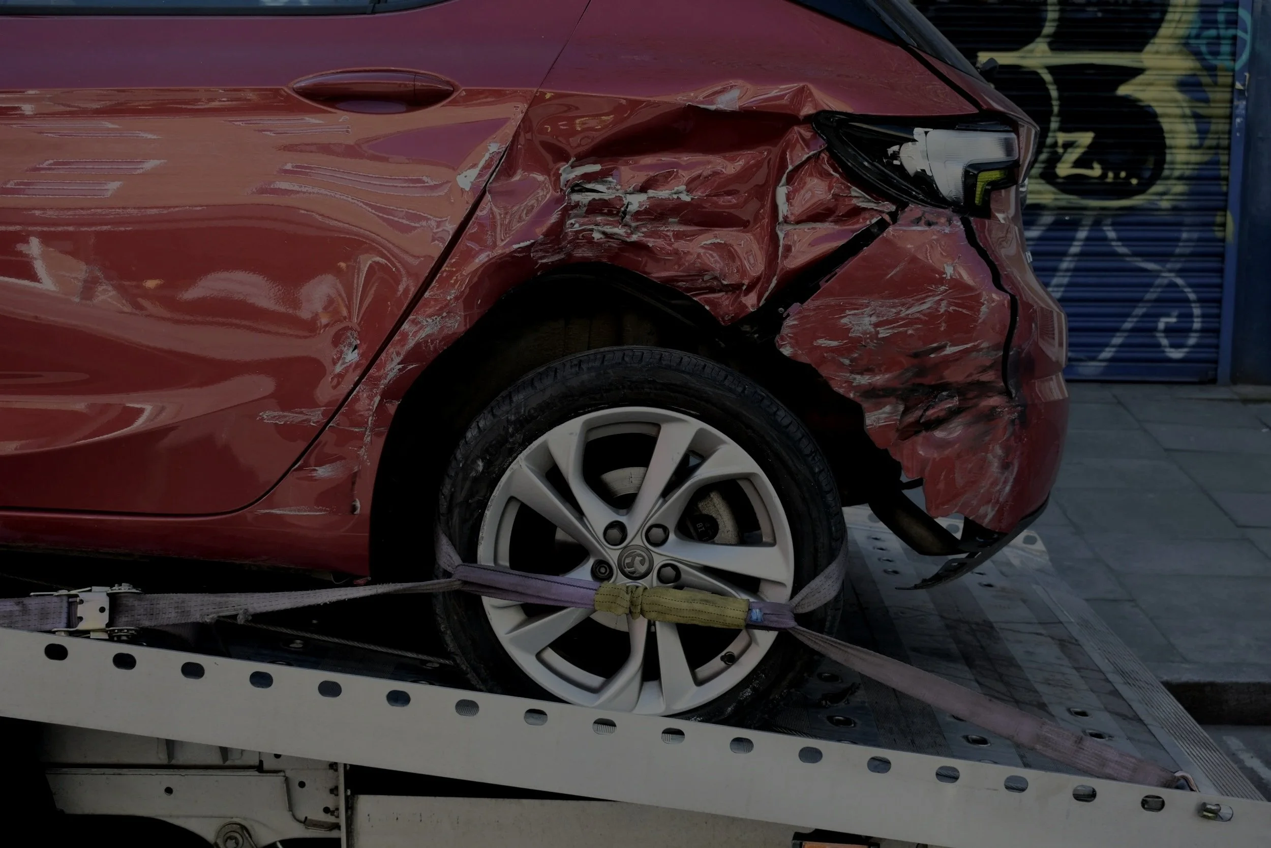 Red car with front-end damage secured on a flatbed tow truck.