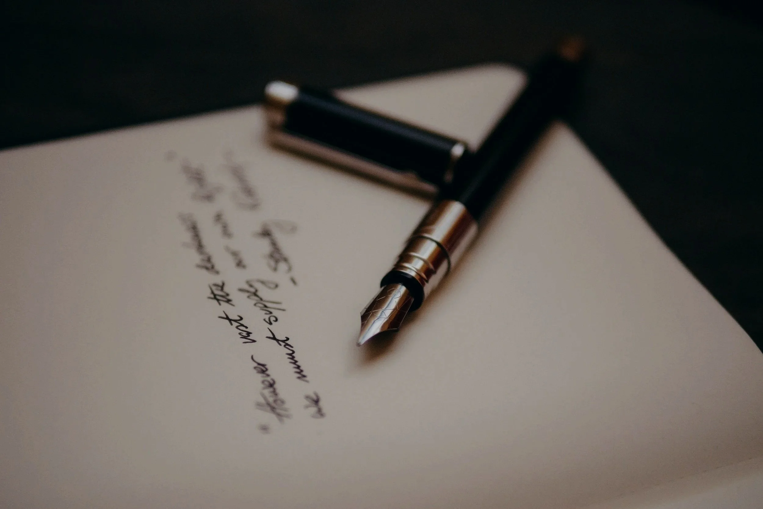 A fountain pen resting on a handwritten letter on a piece of paper.