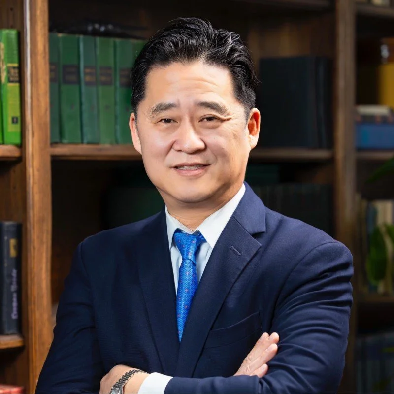 Professional man in suit standing with arms crossed in front of bookshelf.