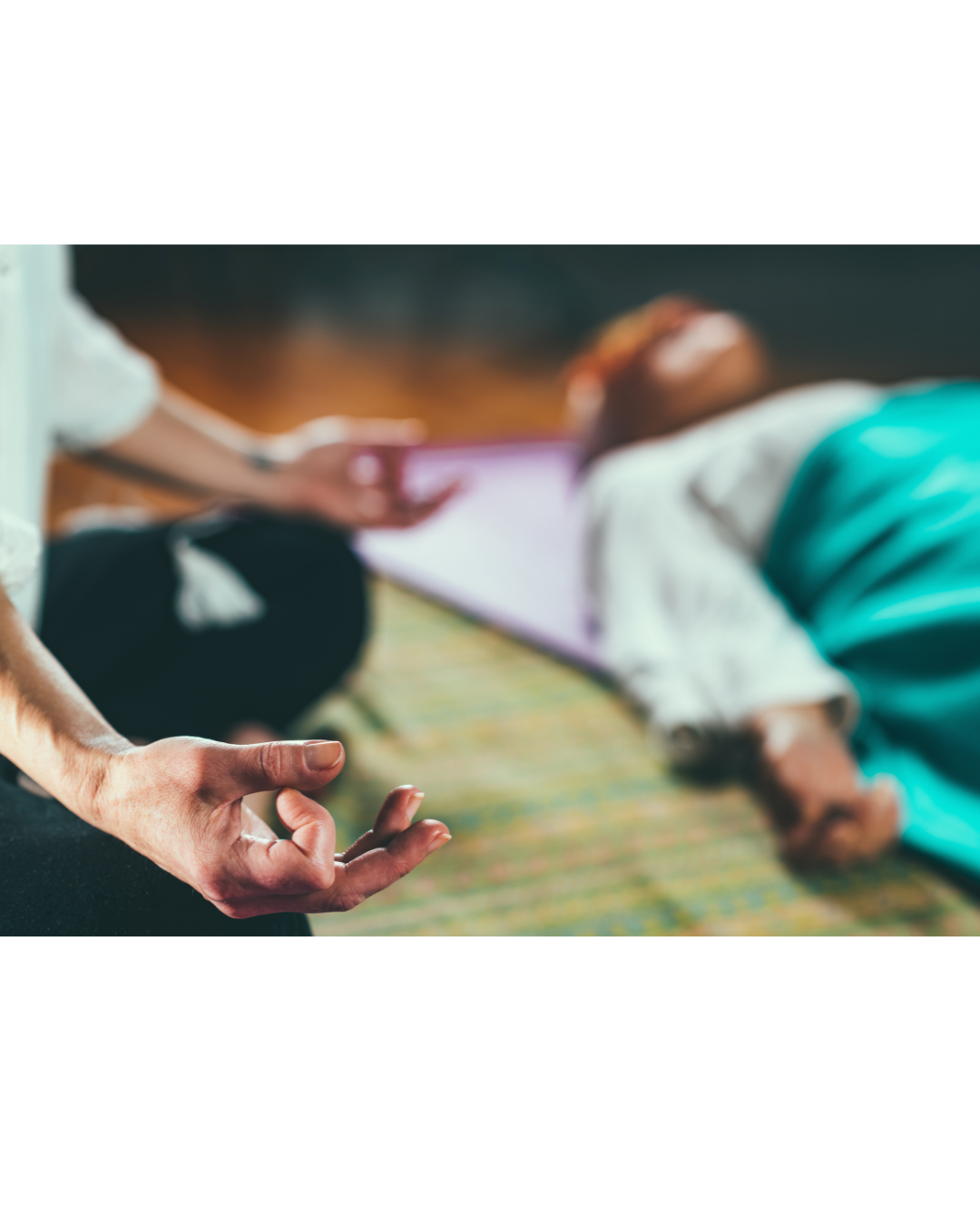 Person practicing meditation while another person lays on the floor receiving a traditional Thai massage in a peaceful setting.
