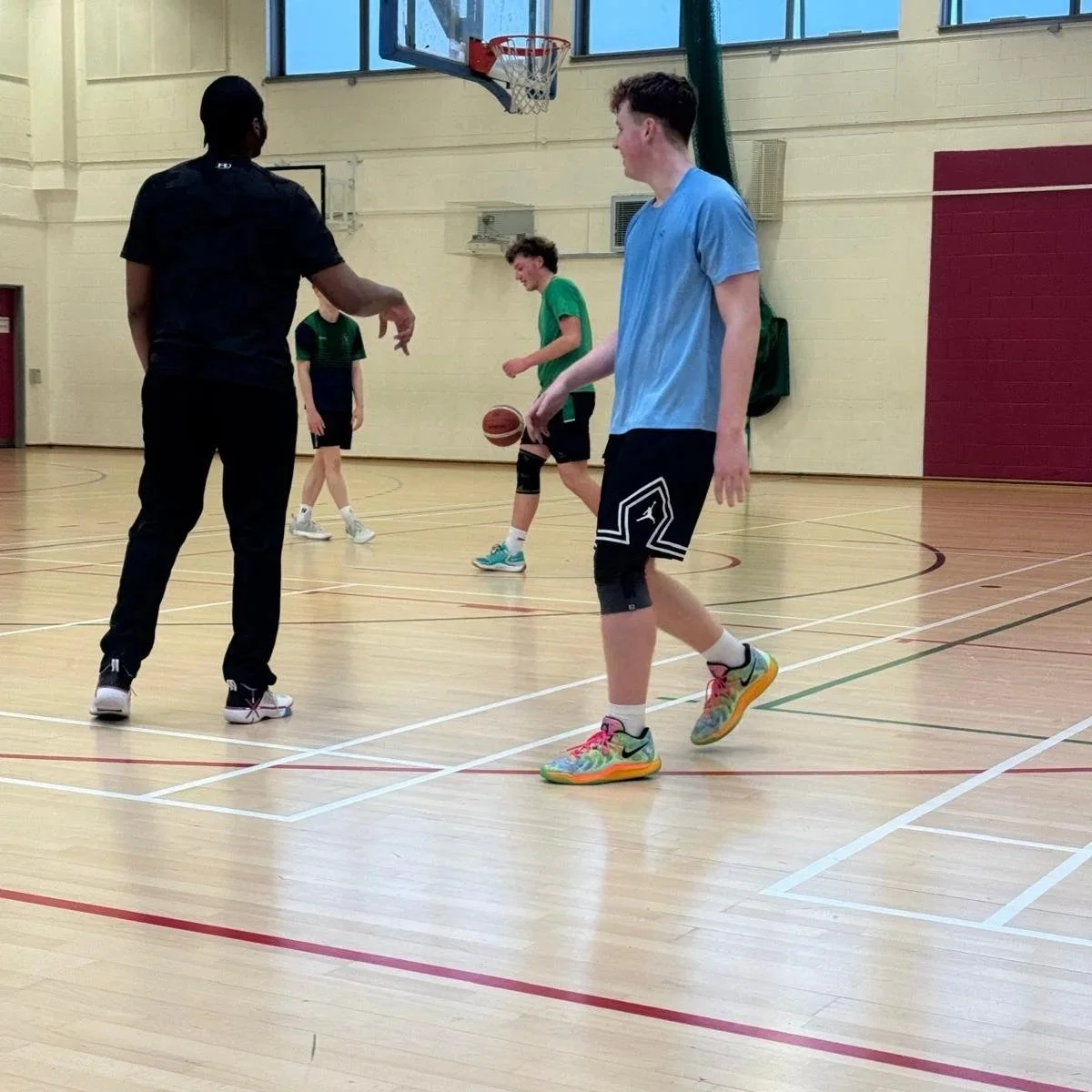 A group of children playing basketball in an indoor gym, with one child dribbling and others standing around.