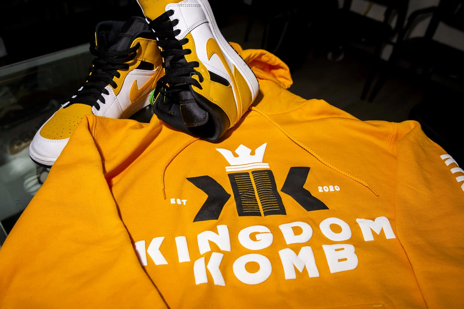 An orange Kingdom KOMB hoodie and a pair of yellow, white, and black sneakers placed on top of the hoodie.