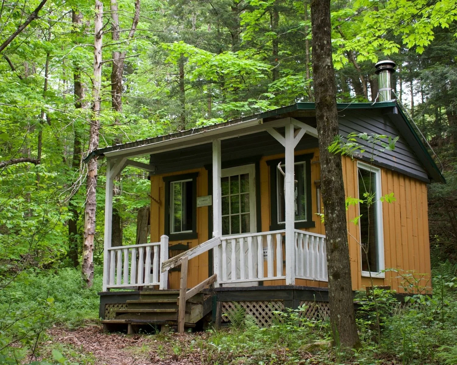 An ochre cabin with a covered deck sits in the woods in Warden, Quebec.