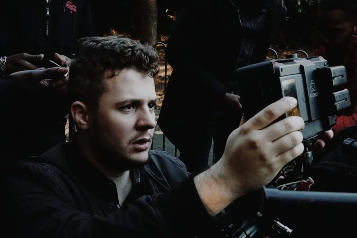 Tristan Fritz at work behind the scenes doing DOP work on Set. A young man with short curly hair holding a professional camera, surrounded by people, outdoors during the evening or night.