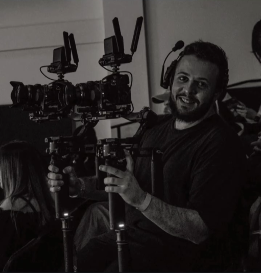 Man operating professional filming equipment with monitors, camera rig, and headphones in a studio or production environment.