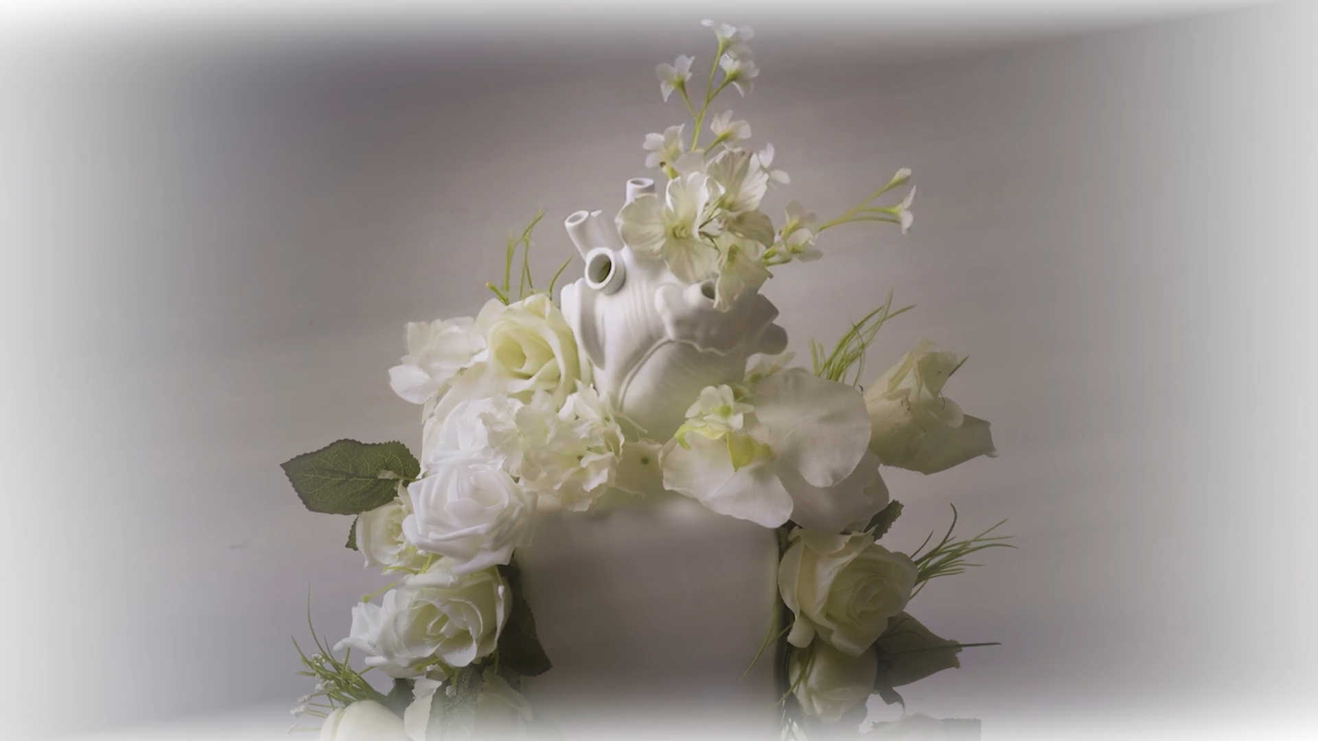 White floral arrangement with a decorative white ceramic heart at the center, set against a plain background.