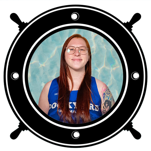 A woman with glasses and tattoos smiling, wearing a blue athletic jersey that says 'Dockyard Tacoma WA', holding a gold helmet, framed by a black and white porthole. 