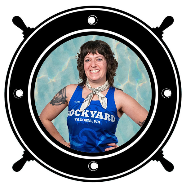 A woman with tattoos on her arms, wearing a blue tank top with 'DOCKYARD' written on it, seen through a circular porthole. 