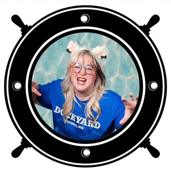 A woman with blonde and brown hair styled with a cat ear headband, wearing a blue sports jersey with the number 80 on her arm, seen through a circular porthole.