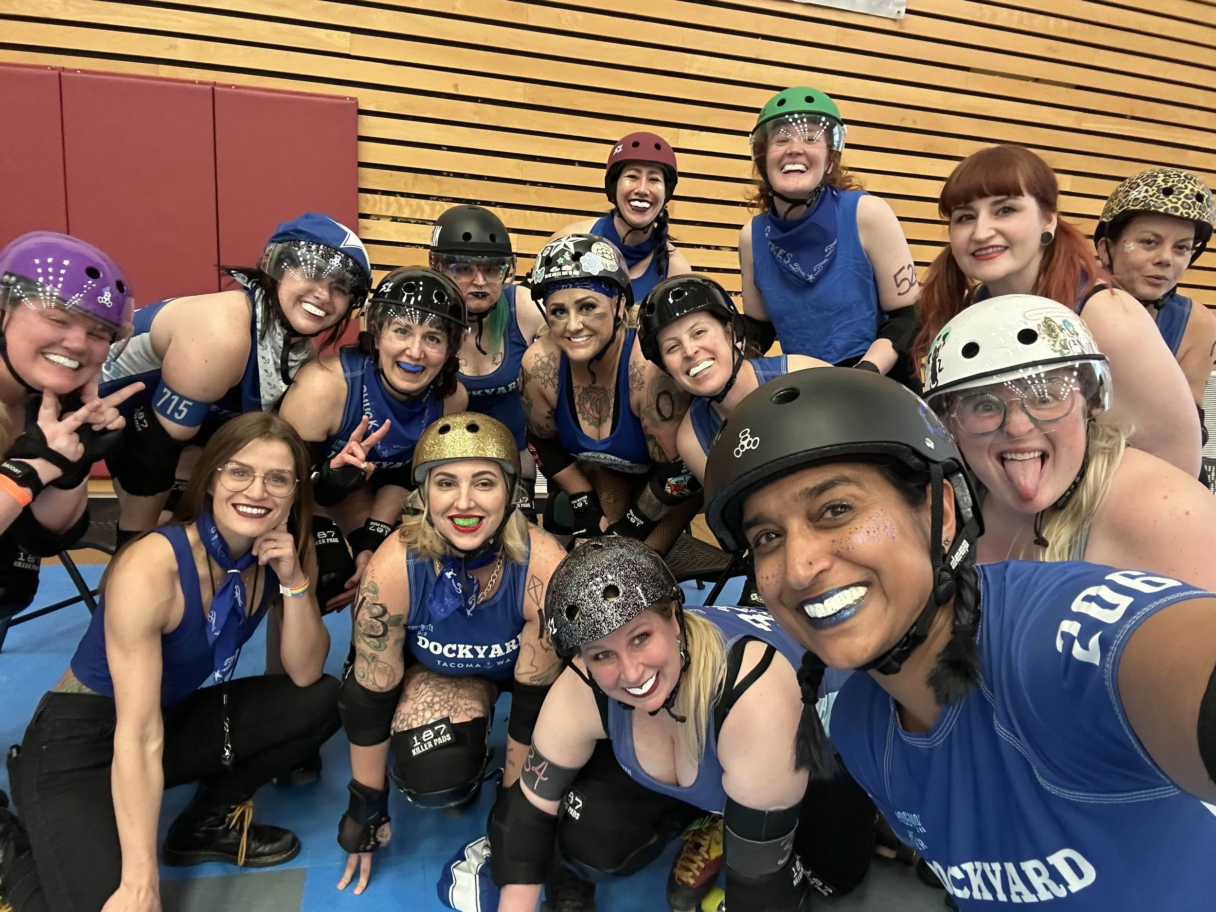 Group of women roller derby players in helmets and uniforms posing together in an indoor rink.
