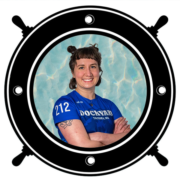 Young woman in blue sports jersey smiling with arms crossed, tattoo on her left arm, seen through a circular porthole.