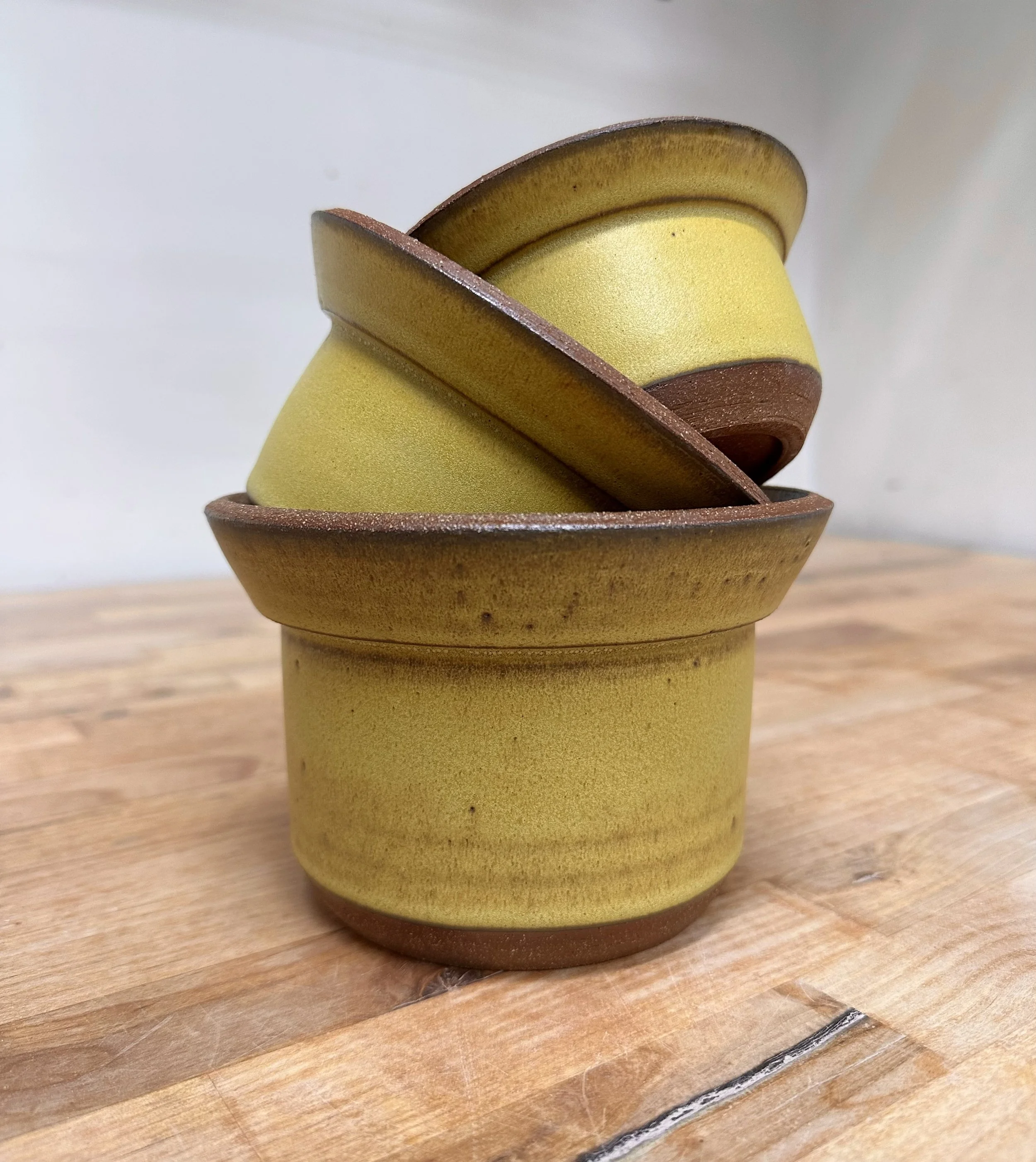 Stack of small ceramic bowls in yellow and brown colors on a wooden surface.
