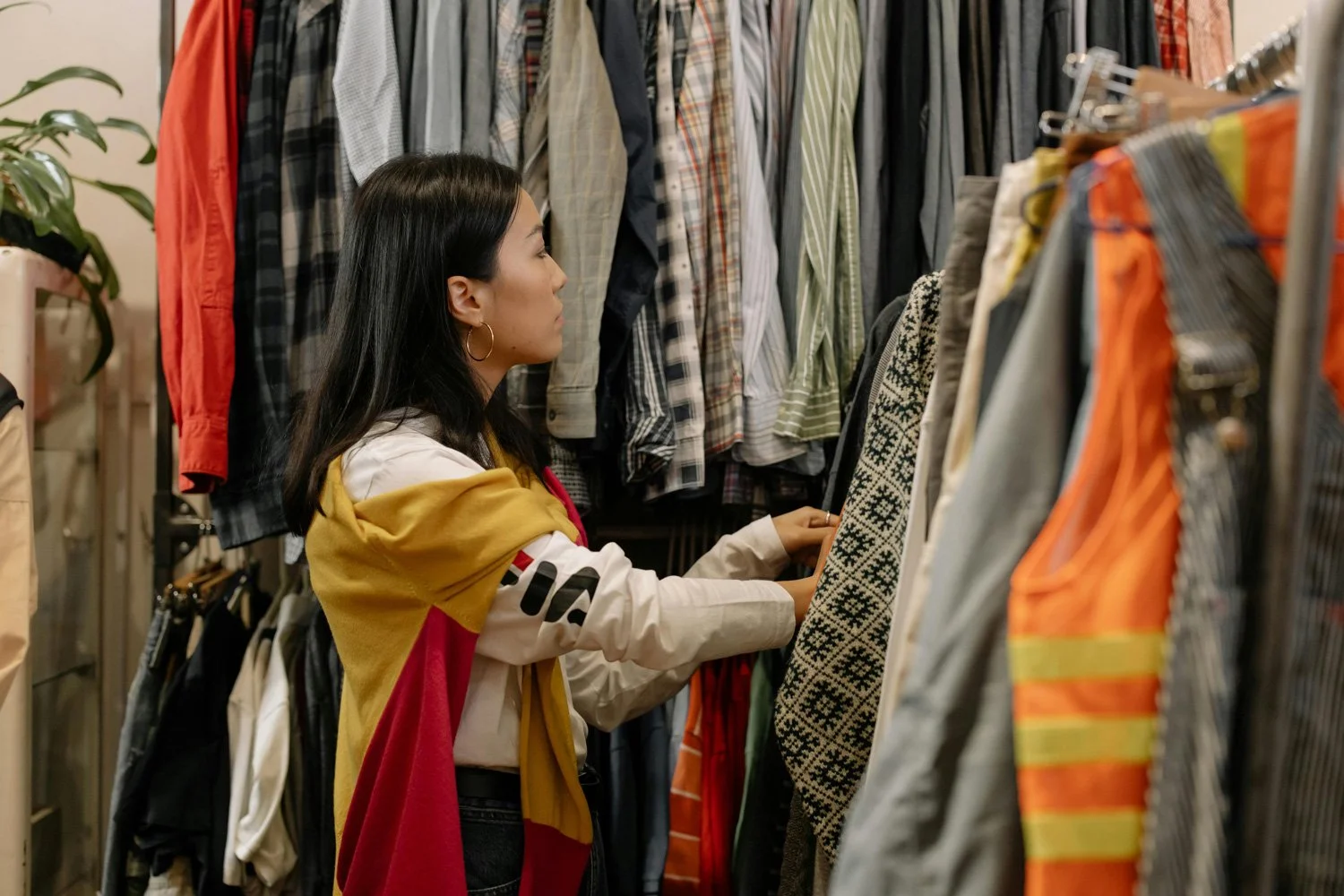 A woman shopping for clothes at a thrift store or clothing store, looking at hanging garments.