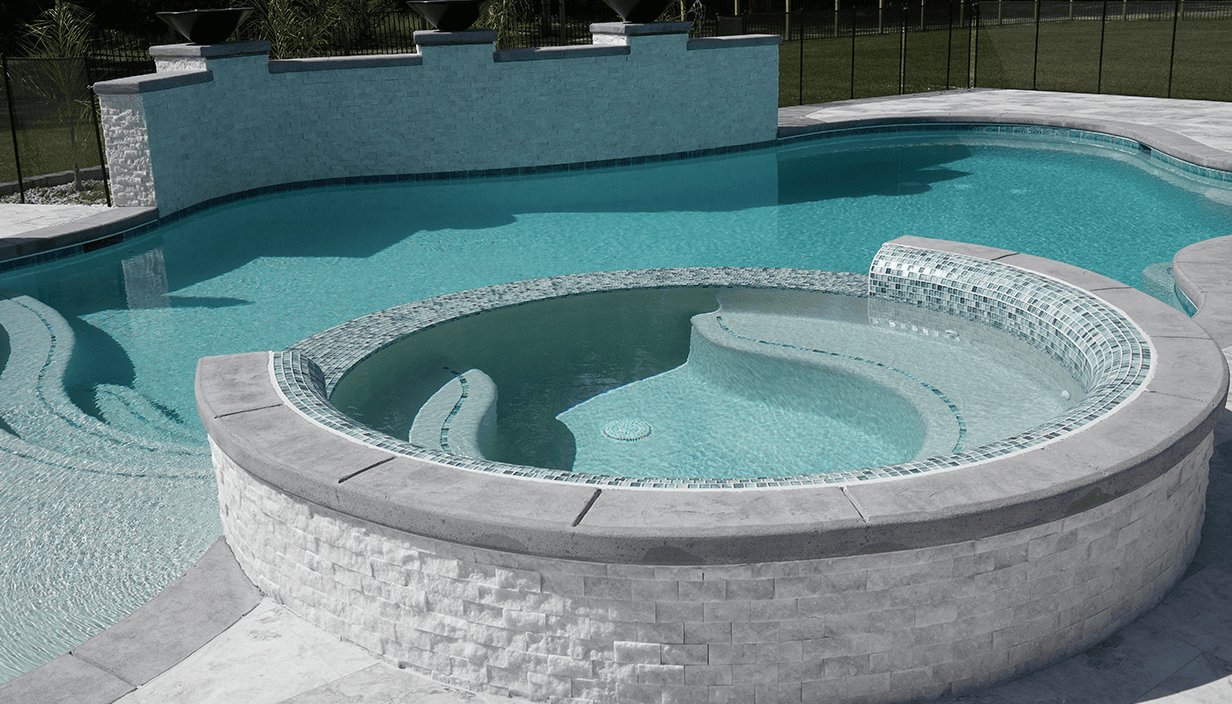 A swimming pool with a connected hot tub, surrounded by a concrete deck and black fence.
