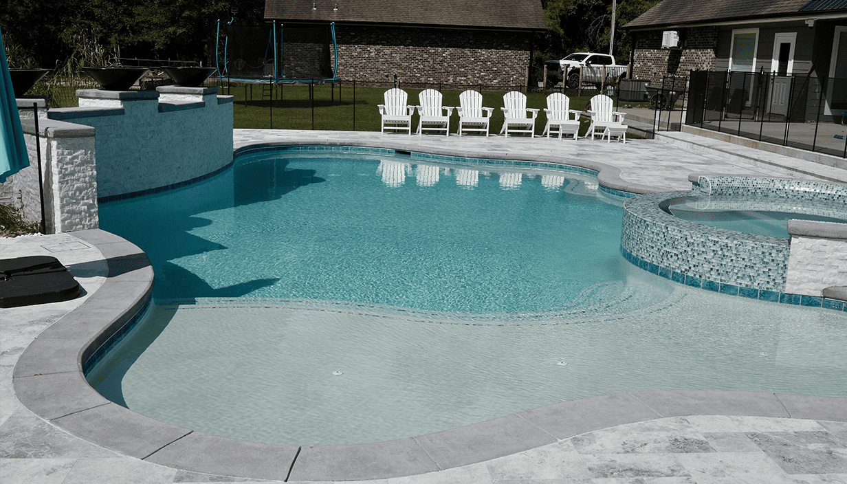 Empty backyard swimming pool with clear water, white lounge chairs, a trampoline, and surrounding houses with fencing.