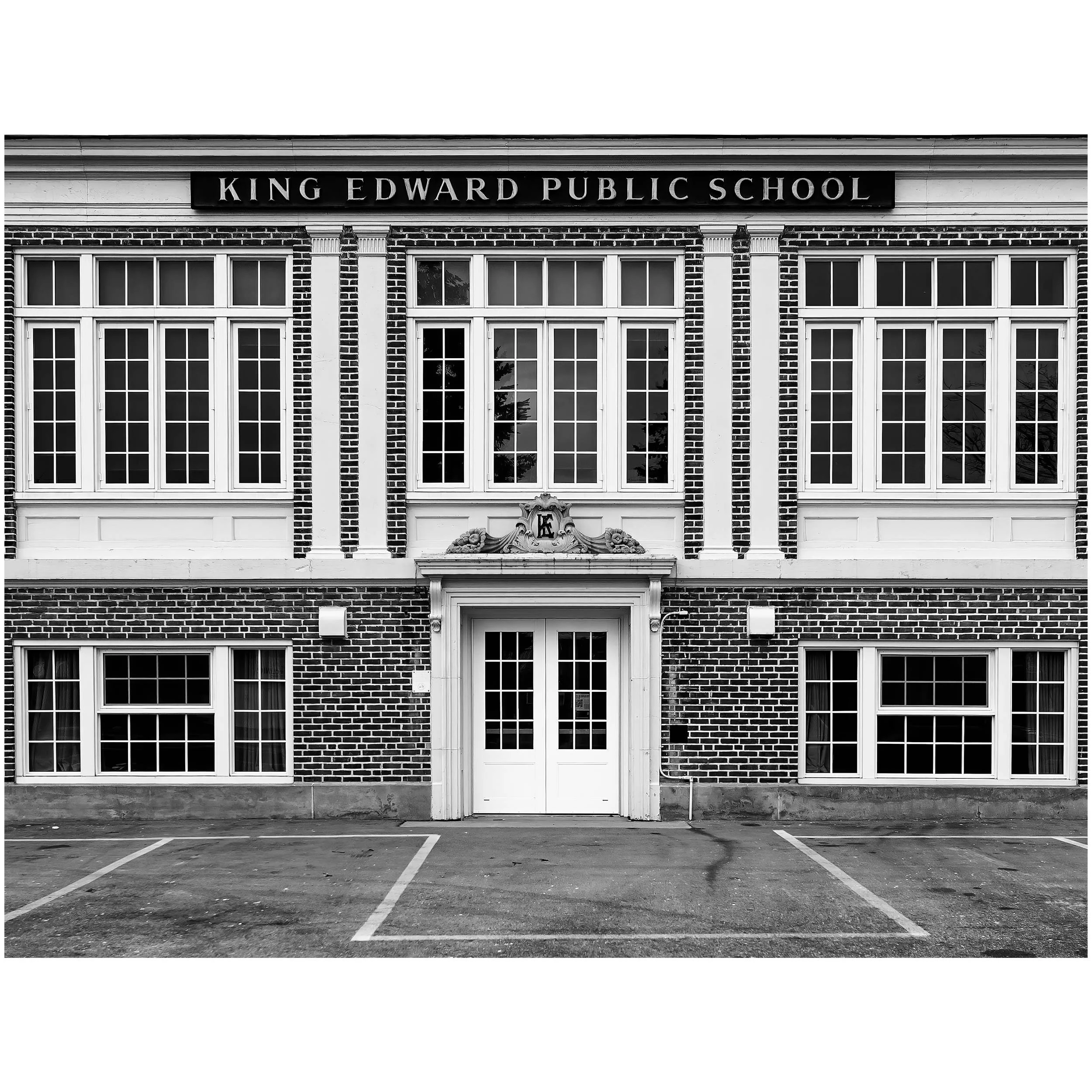 Black and white photo of a school building with large windows, a sign that reads 'King Edward Public School,' and an empty parking lot in front.
