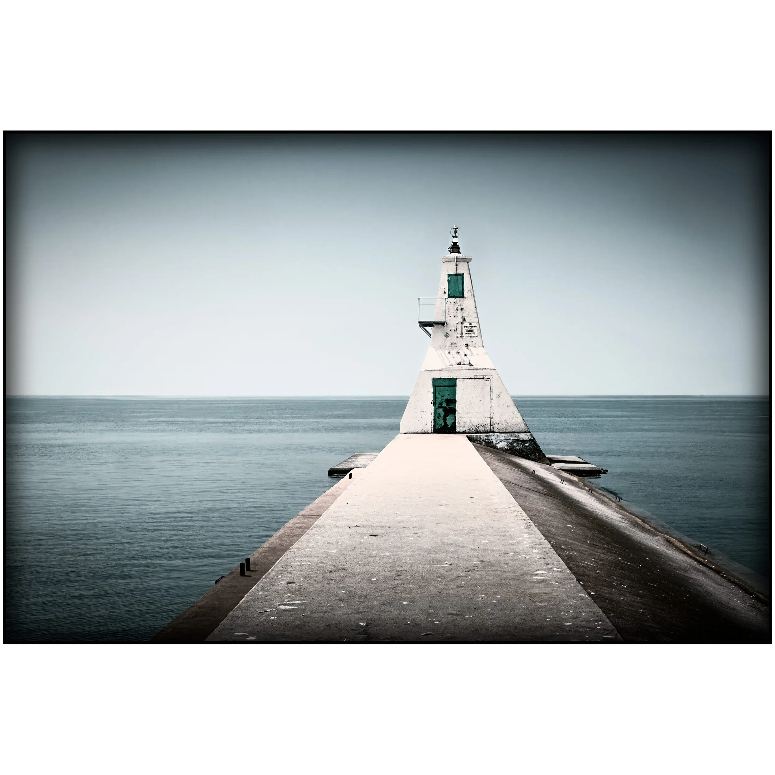 A weathered white lighthouse stands at the end of a narrow concrete pier, with still water on both sides and a quiet horizon behind it.