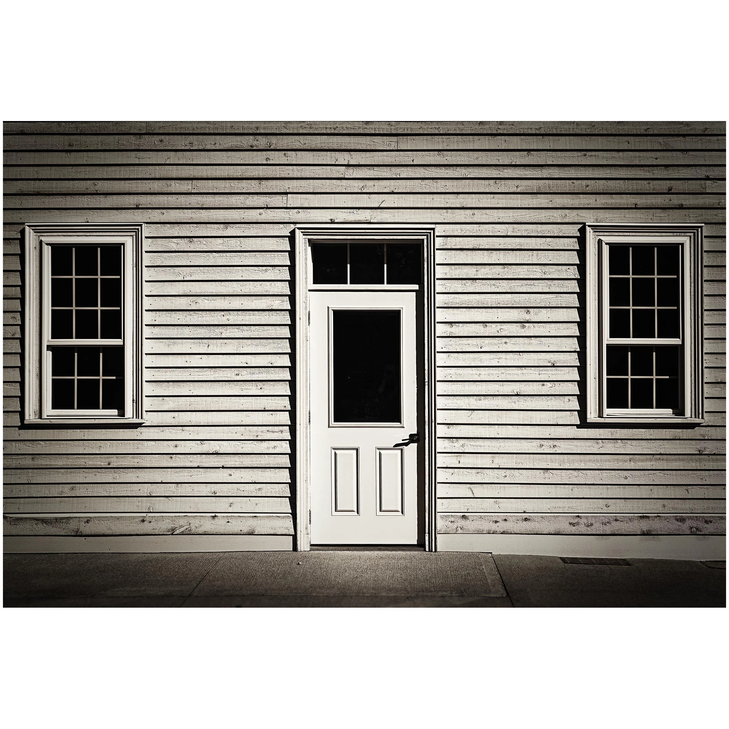 Front exterior of a white wooden house with three windows and a central door, captured at night with shadows cast on the facade.