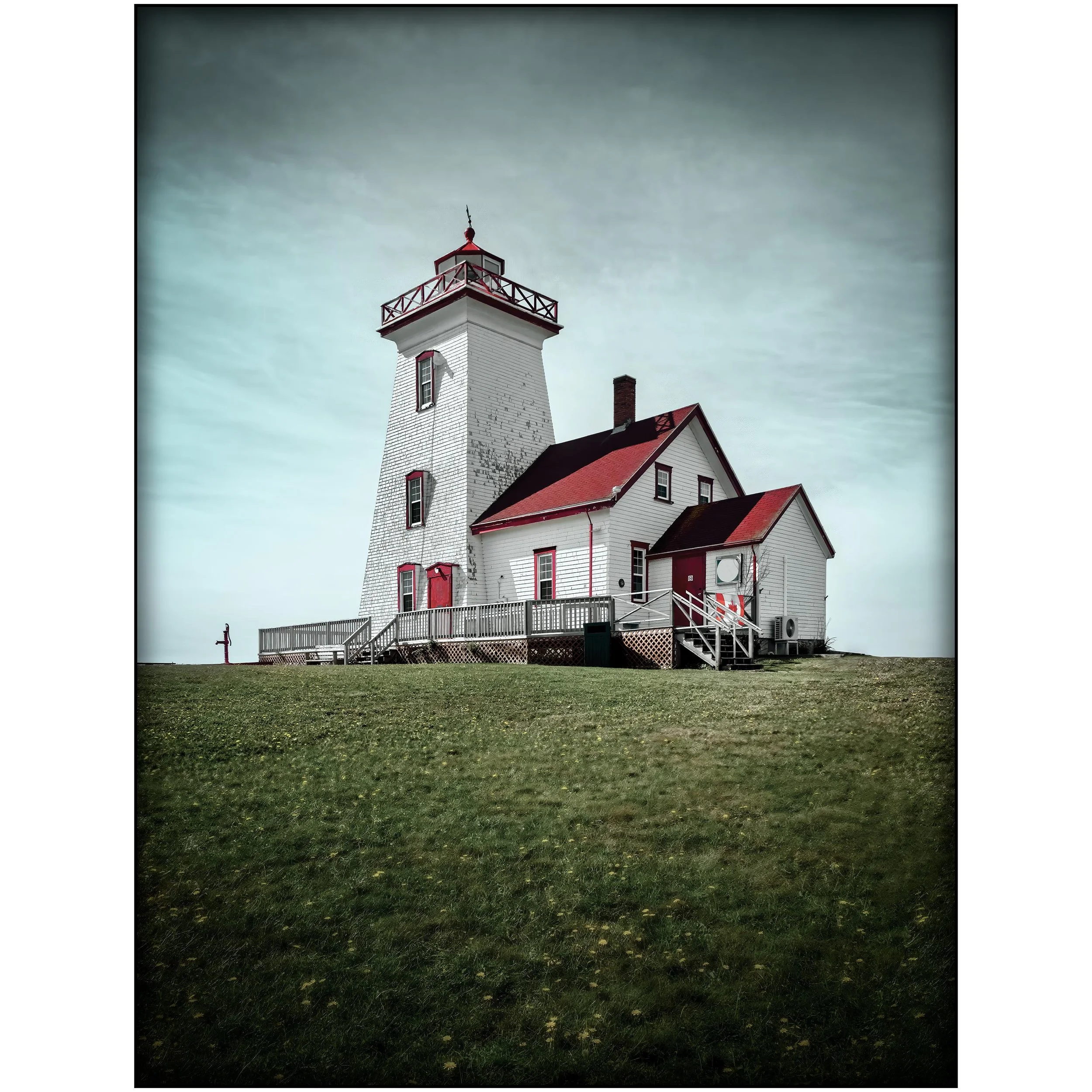 A white lighthouse with red trim and a balcony on top, standing on a grassy area with fallen leaves. The sky is overcast with gray clouds.