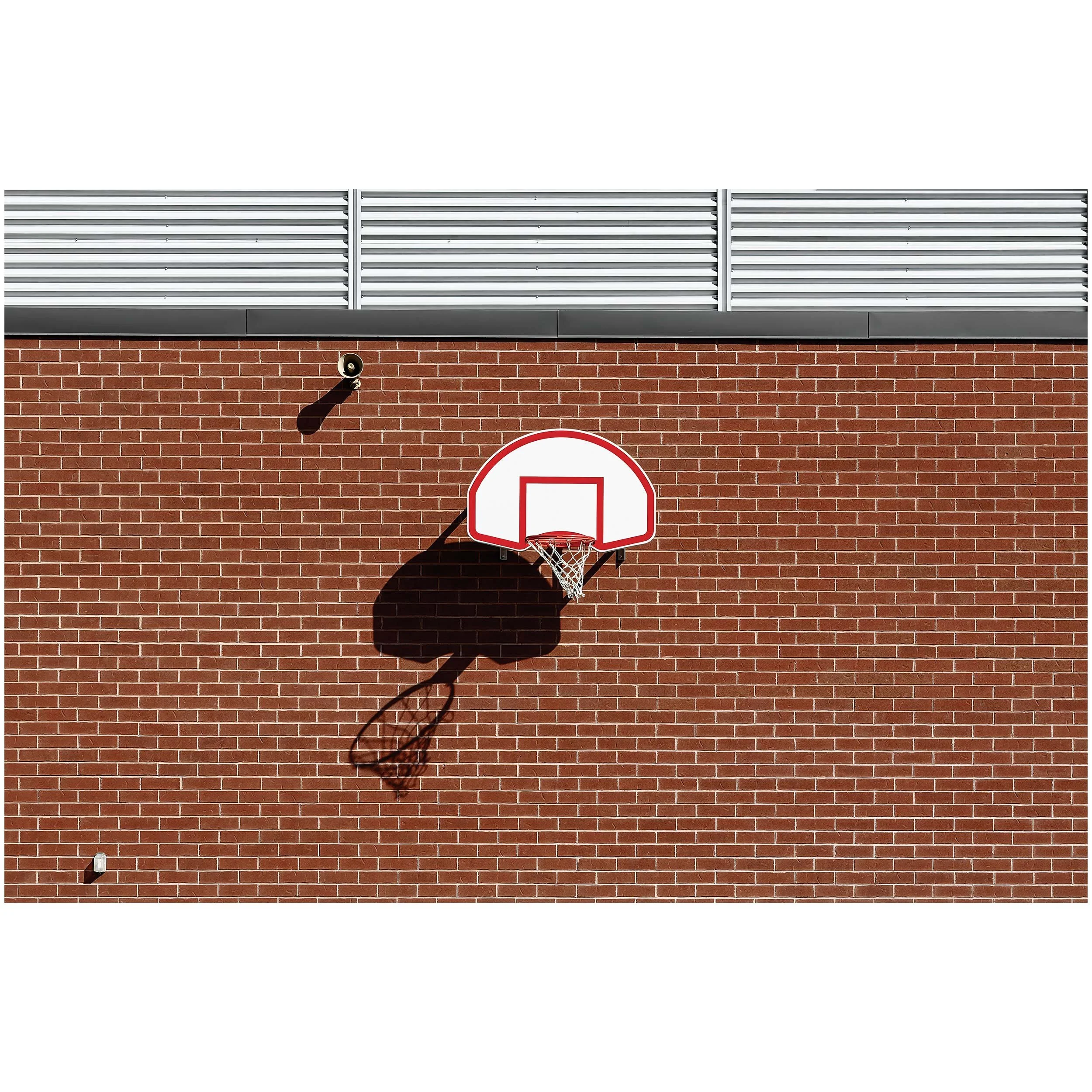 A basketball hoop mounted on a brick wall with a speaker below, against a backdrop of a white sky.