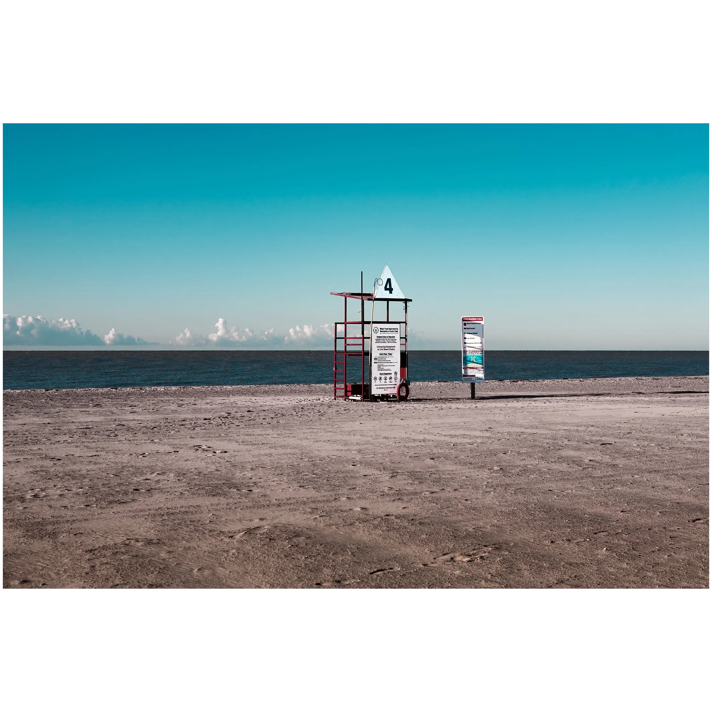 A lifeguard station with a white sail-shaped sign marked number 4, set along a beach with calm ocean waters and cloudy sky in the background.