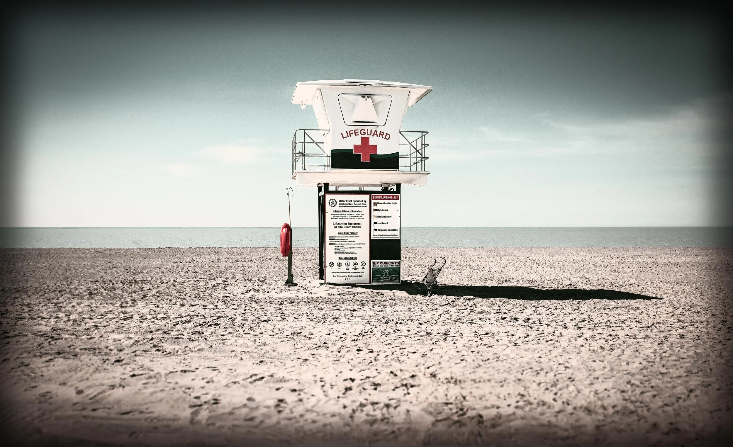 Empty lifeguard tower on a sandy beach with the ocean in the background under a cloudy sky.