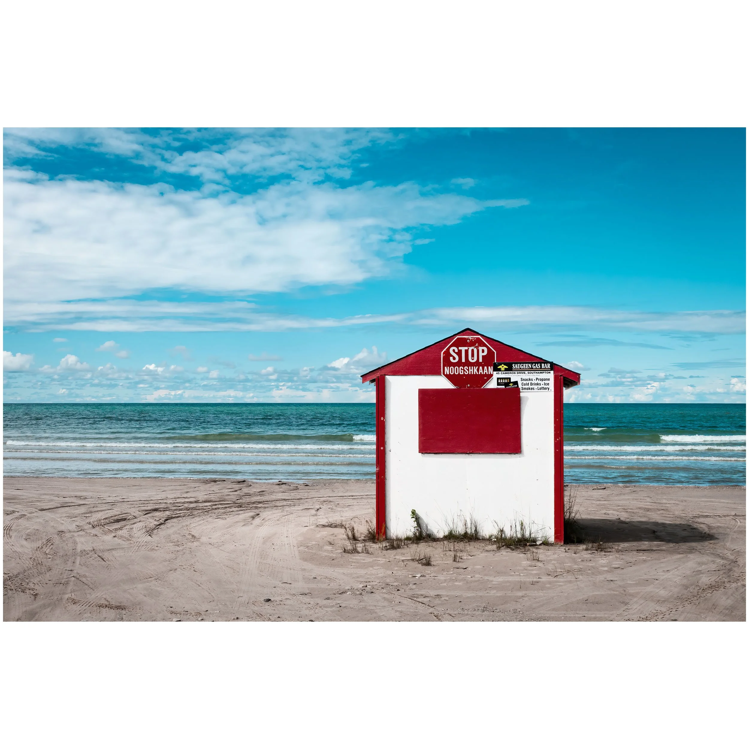A red and white lifeguard stand on a sandy beach with an ocean and a partly cloudy sky in the background.