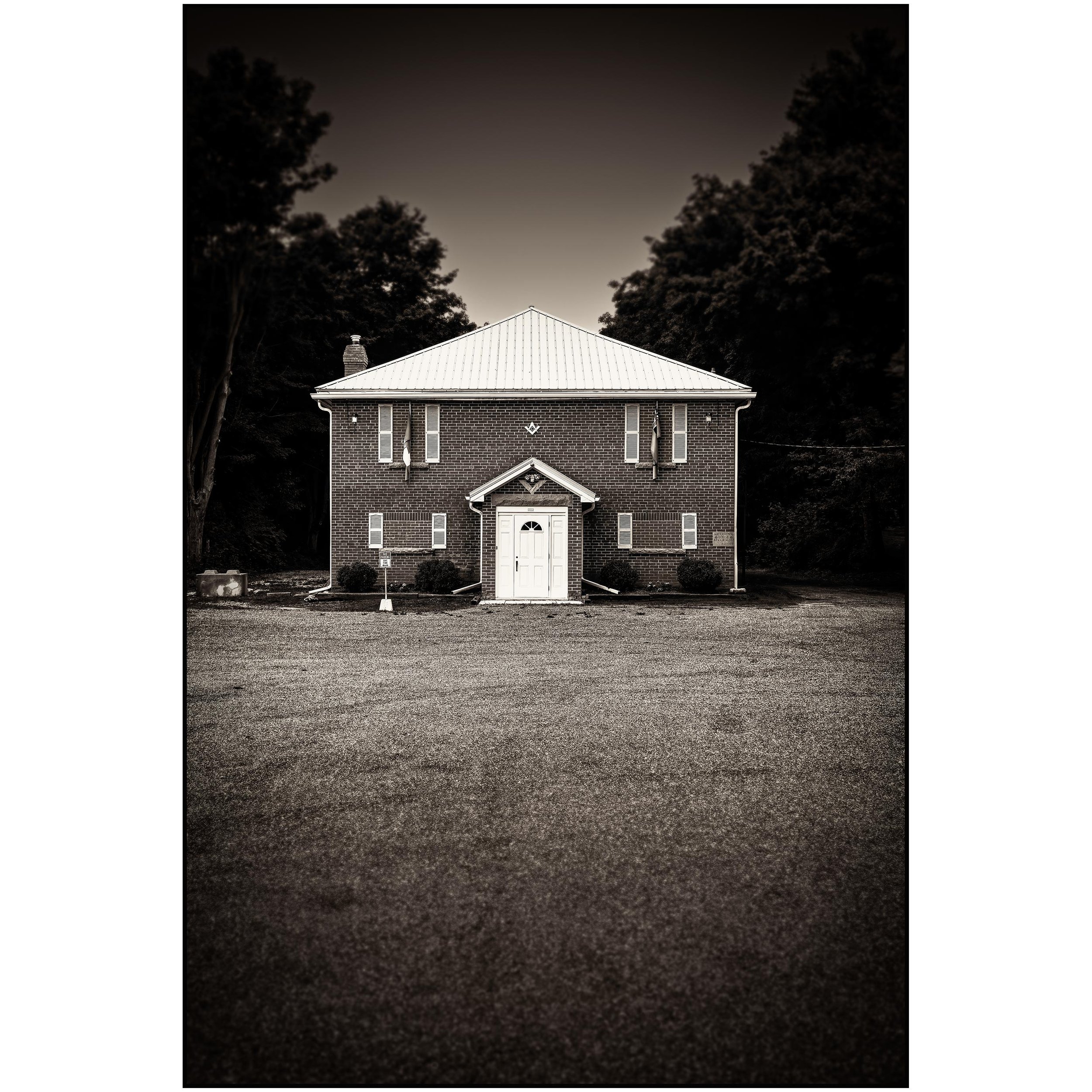 A brick house with a metal roof, front door, and tall trees on either side, taken at dusk or night with a dark sky.