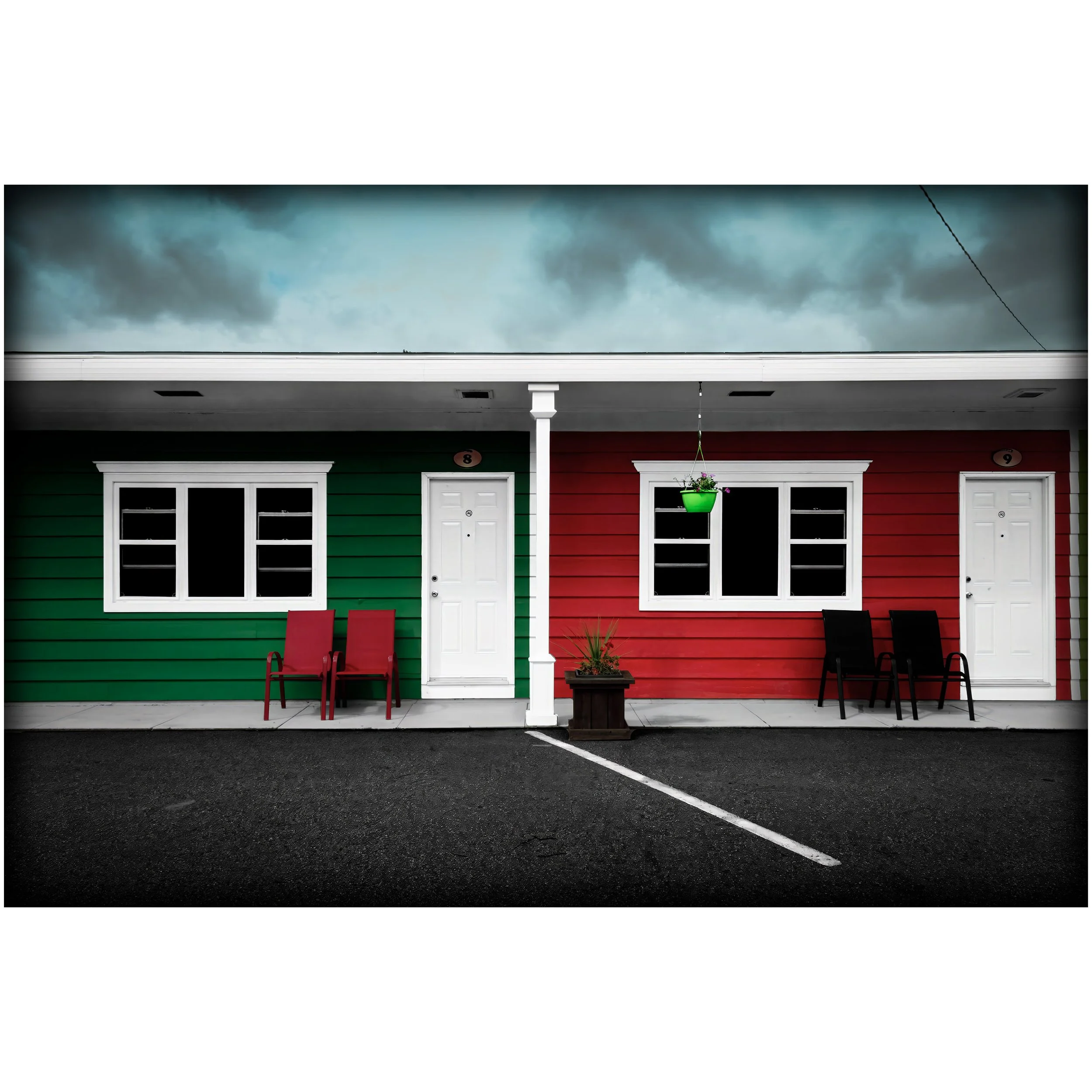 Two brightly painted motel rooms, one green and one red, sit side by side with white doors, empty chairs, and storm clouds overhead.