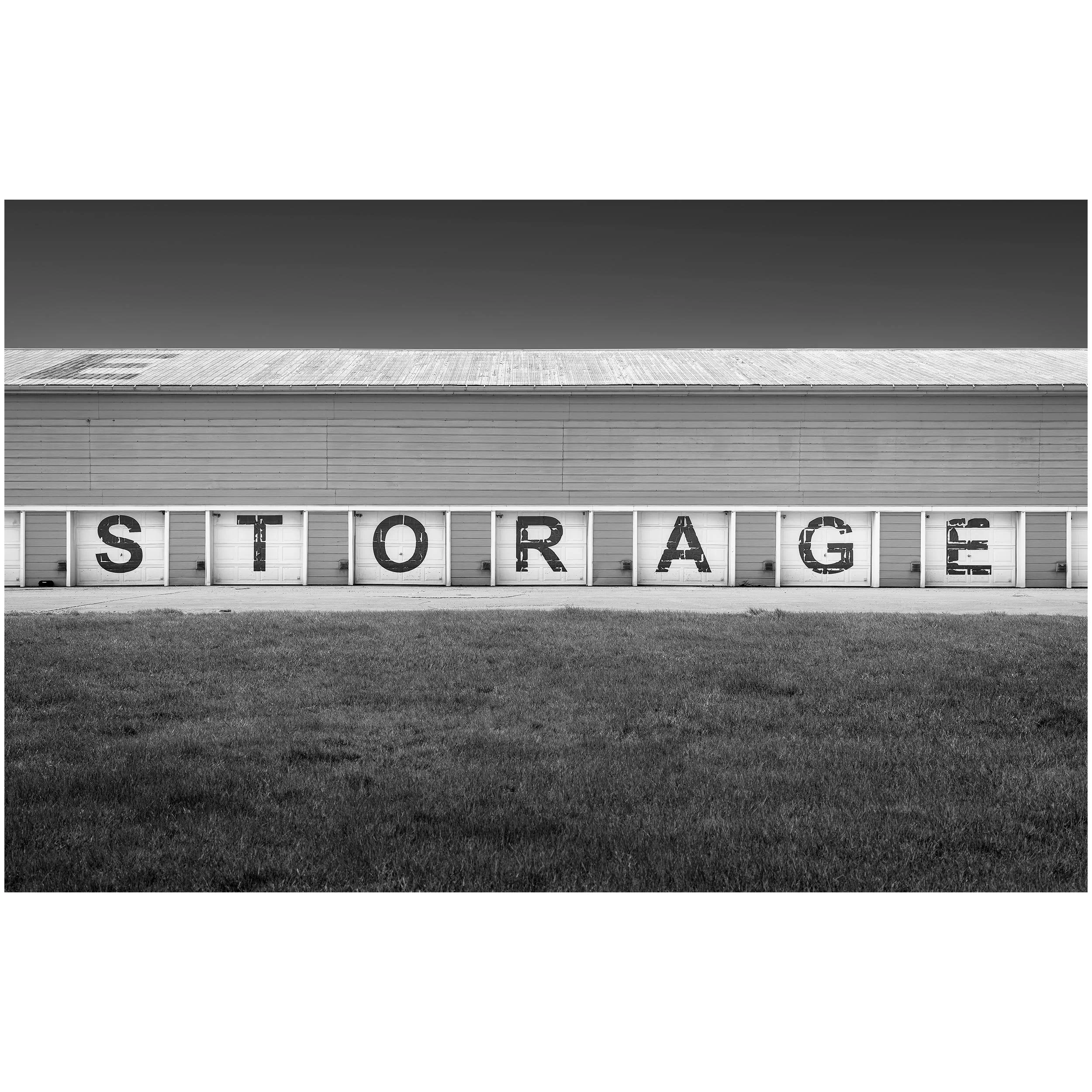 Black and white photo of a large building with the word 'STORAGE' on the side, a grassy area in front.